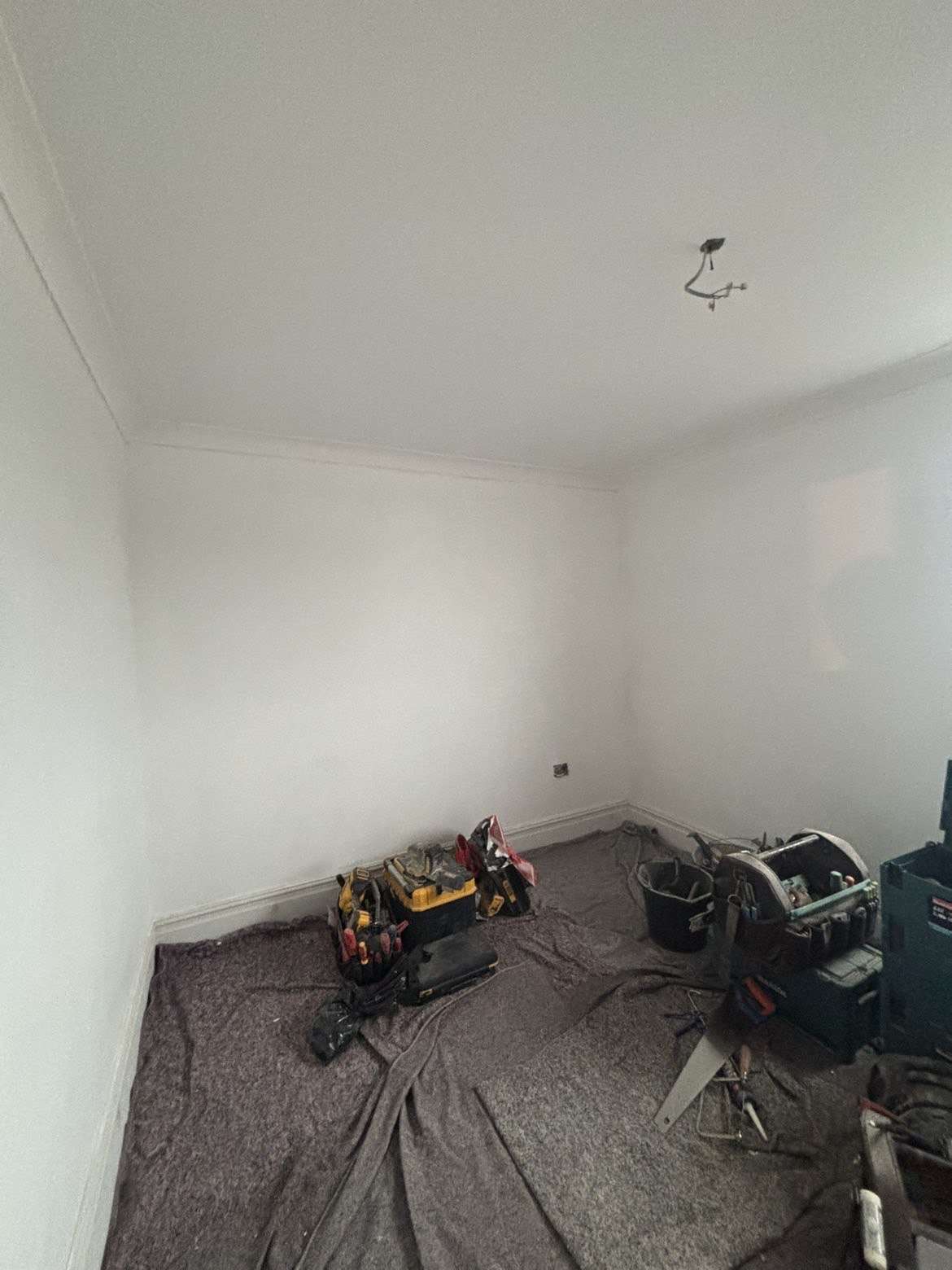 Empty room stripped back and freshly plastered, with dust sheets and power tools on the floor