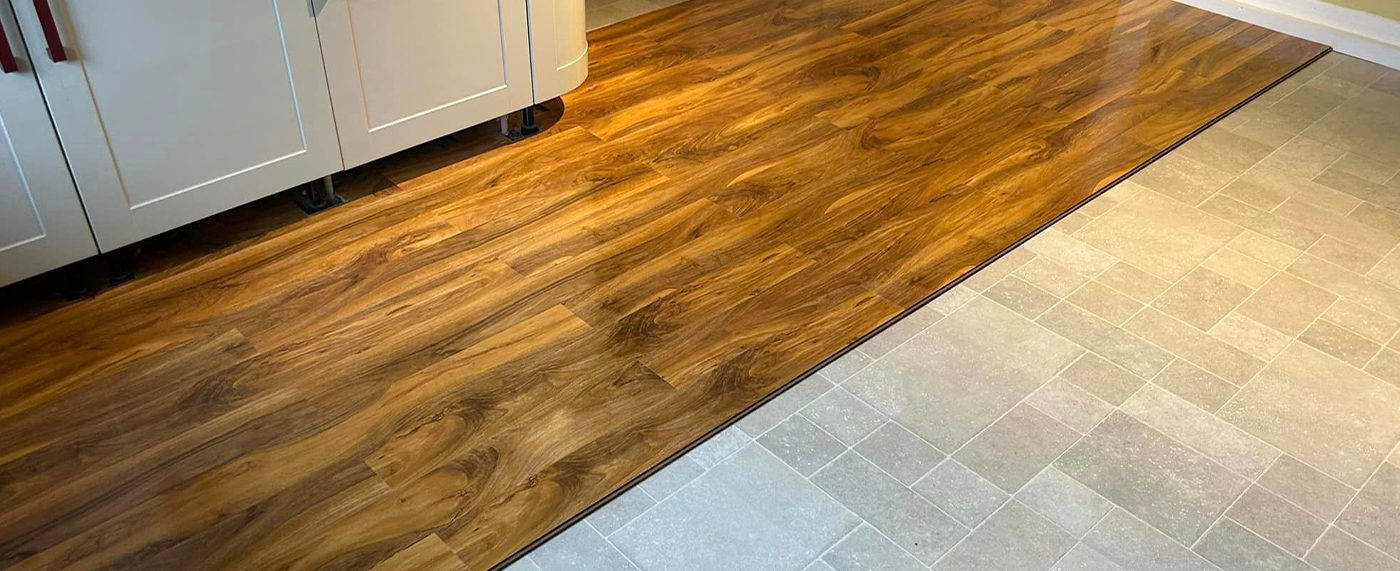 New wood-effect plank flooring meeting stone tiling at a threshold in a fitted kitchen