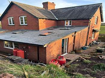 Red brick house with the roof stripped back to battens during roofing works